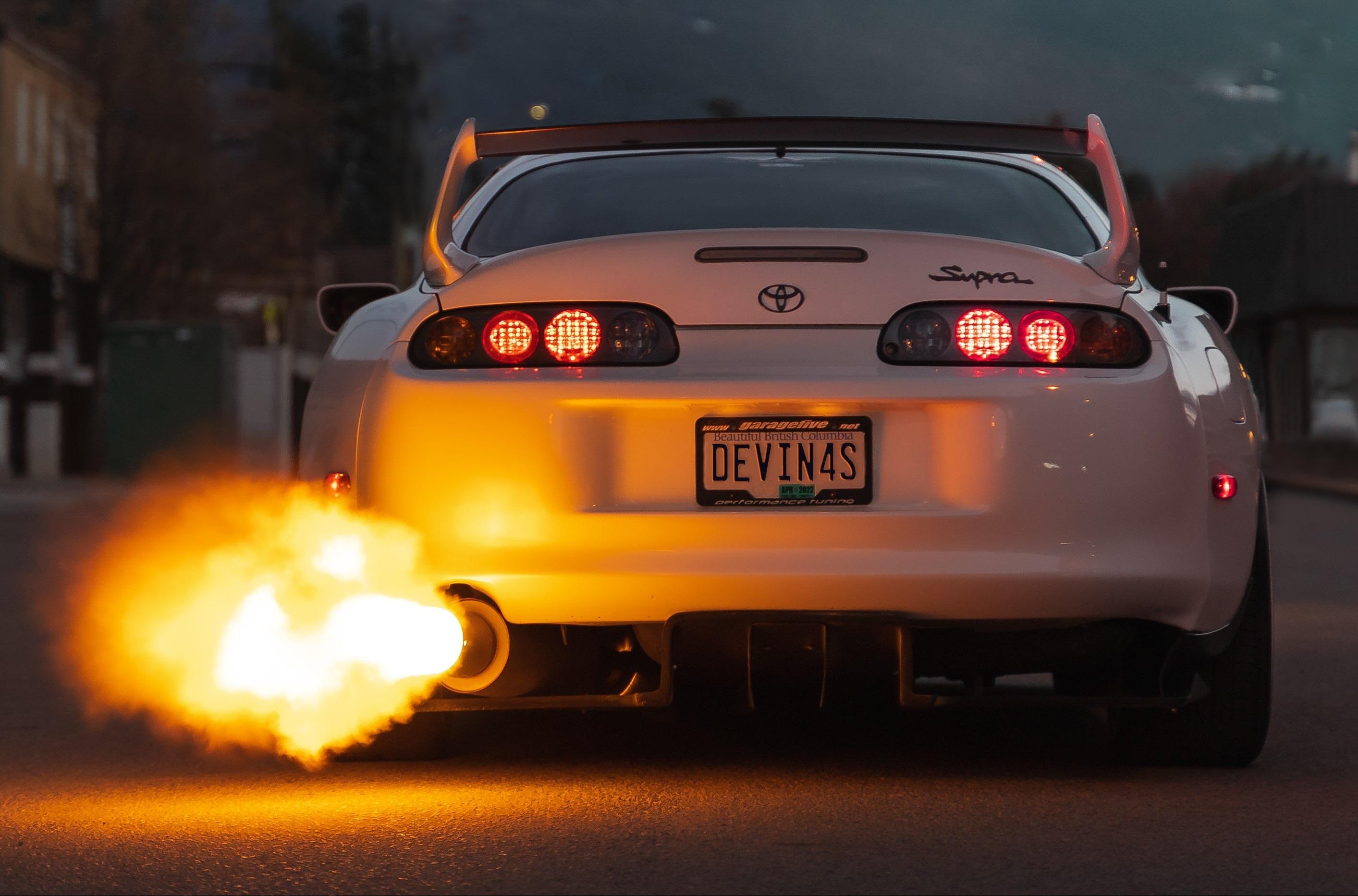 White Toyota Supra with exhaust flames on a dark road